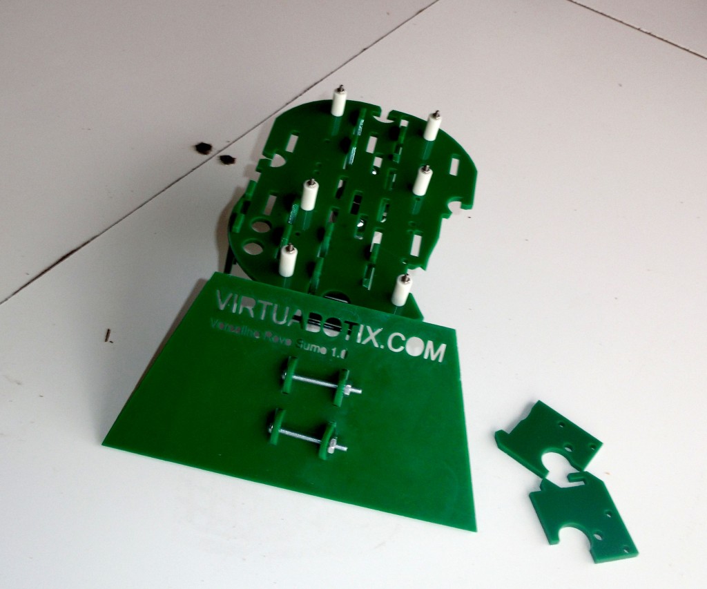 A broken green acrylic Versalino Rove Gumo robot chassis kit in pieces on a white floor after a fall.