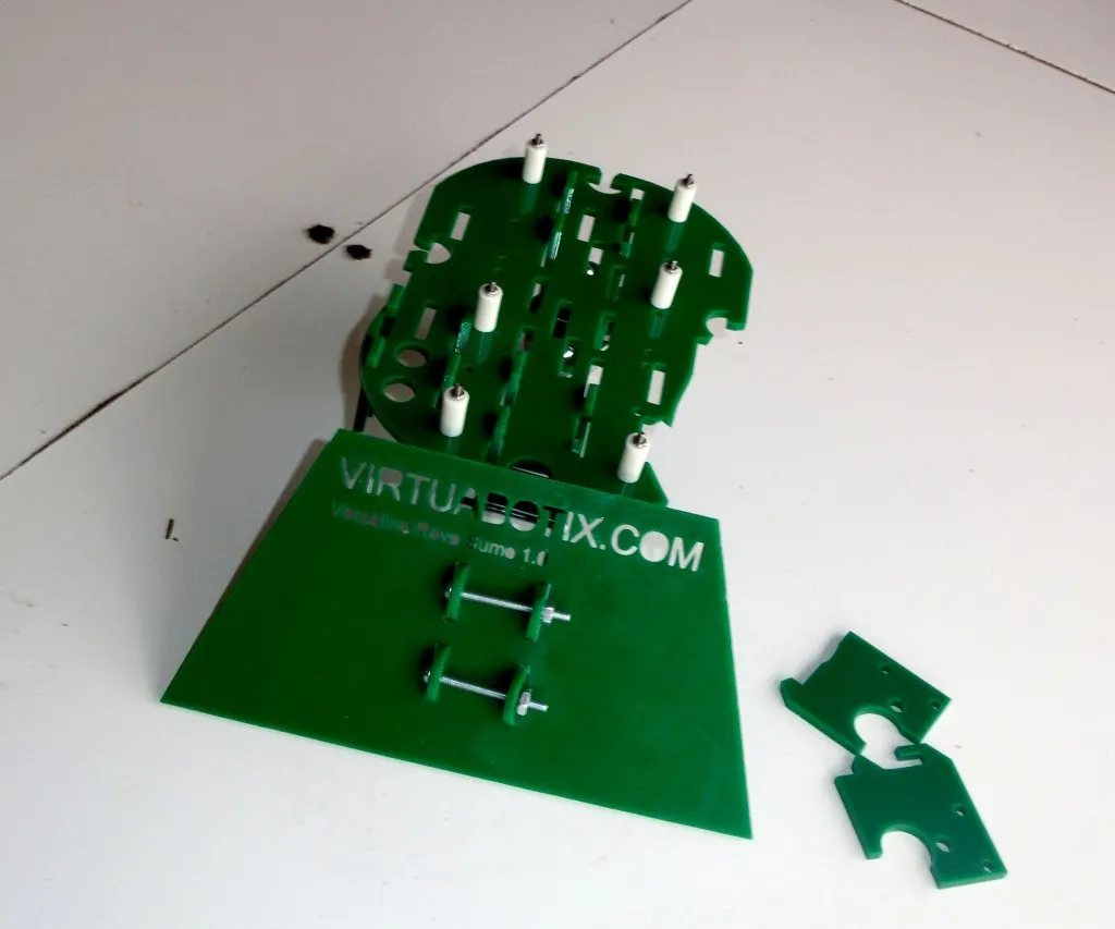 A broken green acrylic Versalino Rove Gumo robot chassis kit in pieces on a white floor after a fall.